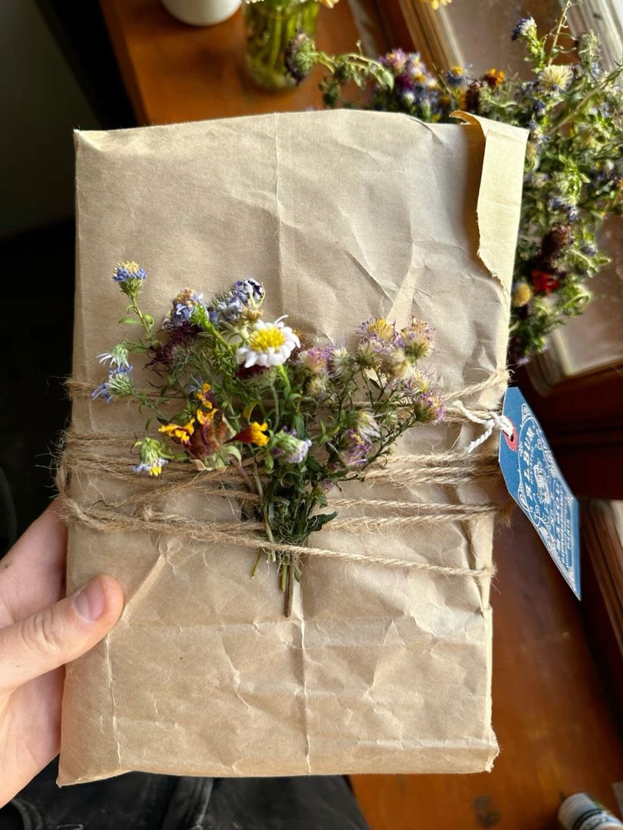 Pacote de papel kraft amarrado com barbante e um buquê de flores do campo